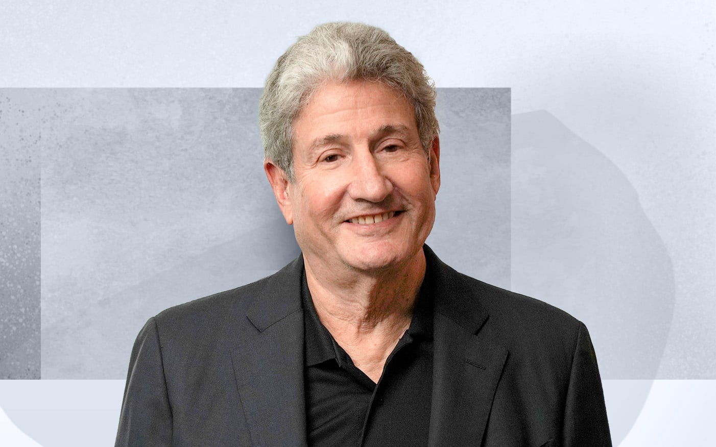 Roger Solomon who is smiling in a black suit and shirt, standing against a simple gray and white background.