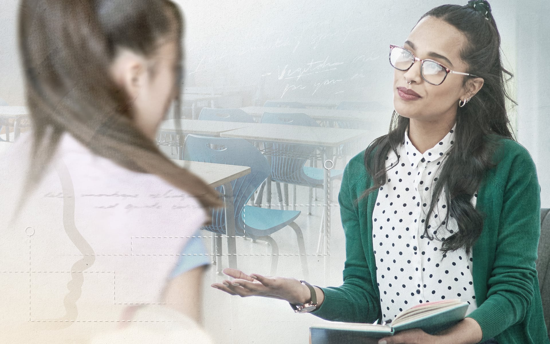 A woman with long dark hair and glasses sits in conversation with another person, who is partially visible. She is wearing a green cardigan over a white polka dot blouse and holding an open notebook. The background features classroom desks.